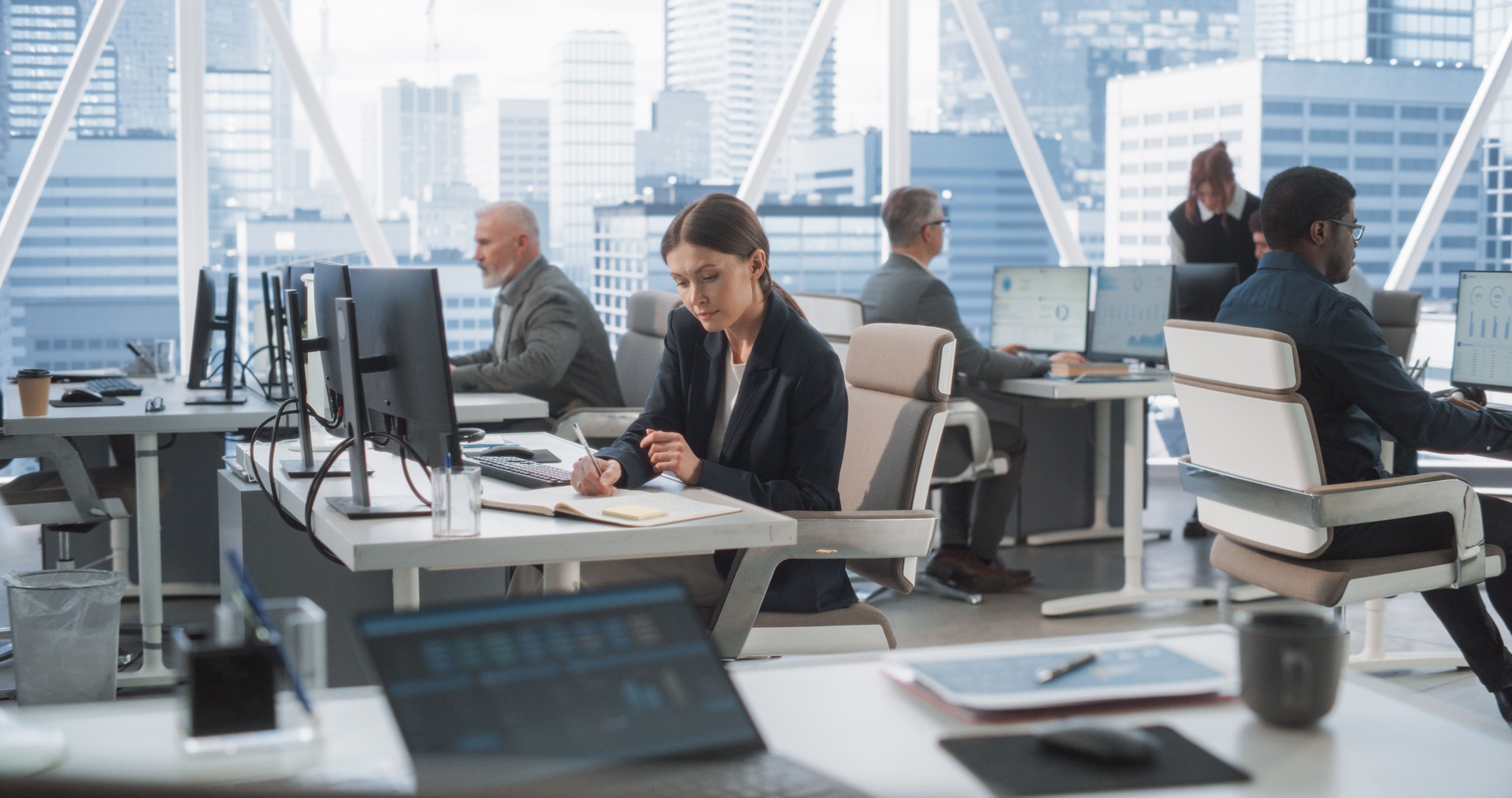 In Big Corporate Skyscraper Office: Beautiful Caucasian Female Business Manager Using Computer, Businesspeople and Experts Working Around Her, Analysing Statistics, Commerce Data, and Marketing Plans.