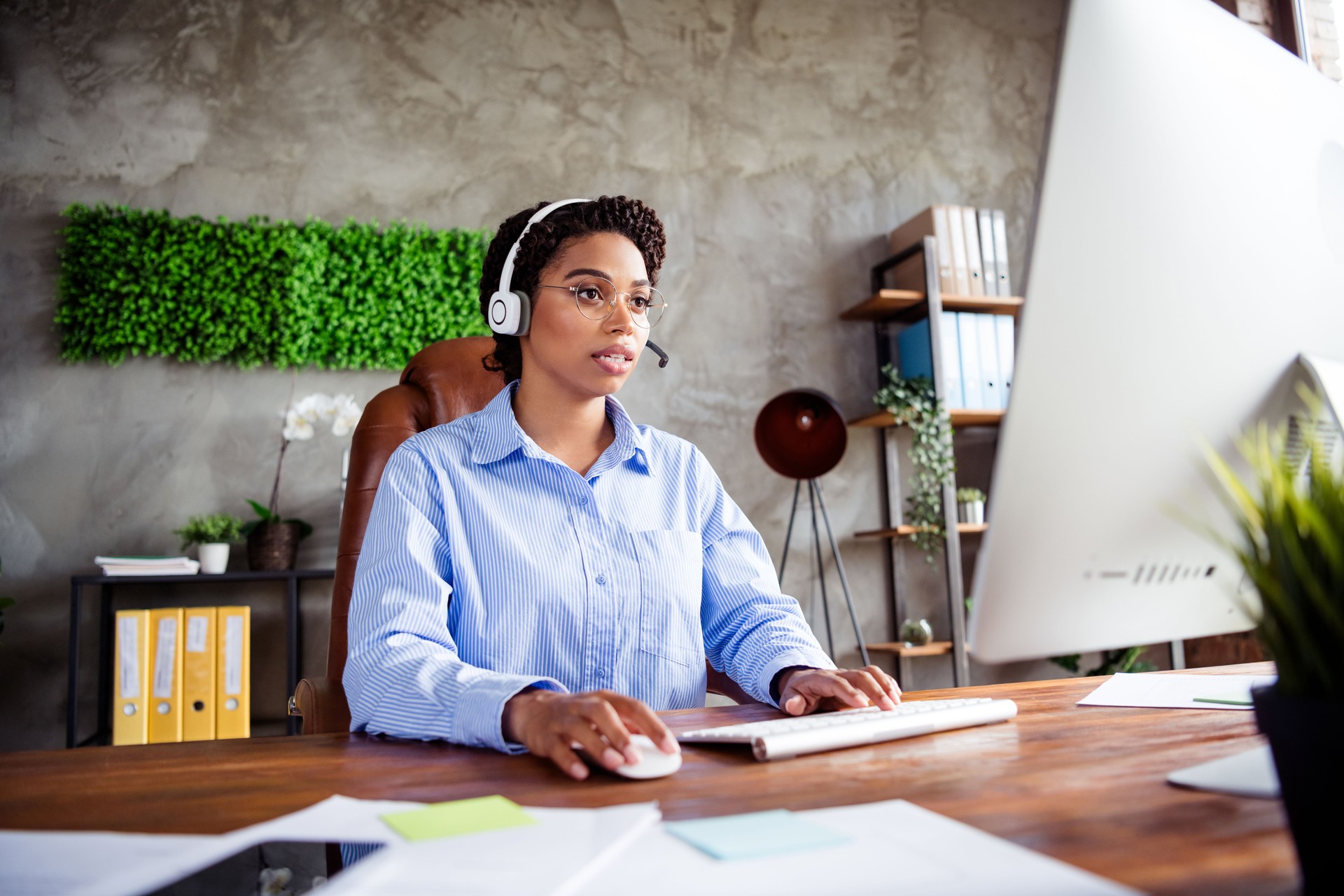 Young businesswoman in a formal blue blouse working in an office environment with headset, showcasing corporate style and efficiency